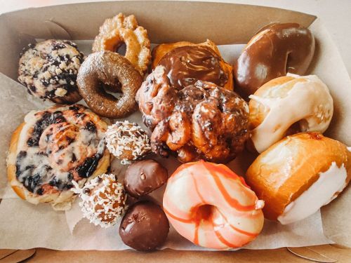 A variety of colorful donuts and pastries arranged in a box, including glazed, chocolate, and frosted options.