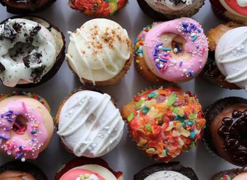 A colorful assortment of decorated cupcakes with various toppings and frosting, arranged in a grid pattern.