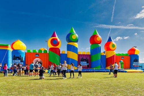 A colorful inflatable bounce house with people enjoying a sunny day in a grassy field.