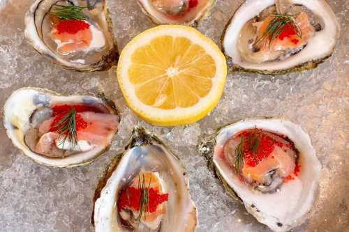 A platter of oysters on ice, garnished with dill and red caviar, with a lemon slice in the center.