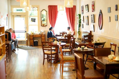 Cozy café interior with wooden tables, chairs, and patrons enjoying drinks by the window, adorned with warm decor.