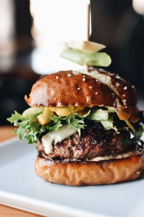 A close-up of a juicy burger with lettuce, pickles, and sauce, served on a toasted pretzel bun.