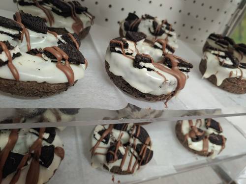 Delicious donuts topped with white icing, crushed Oreos, and drizzled chocolate, displayed on a shelf.