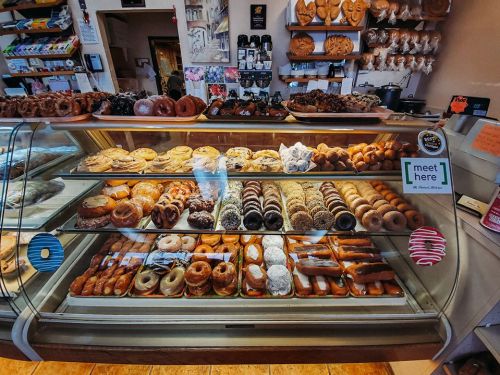 A display case filled with various donuts and pastries in a cozy bakery setting.