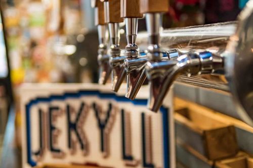 Close-up of beer taps with a "Jekyll" sign in the background, showcasing a vibrant bar atmosphere.