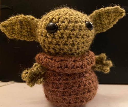 A small, crocheted figure with large ears, wearing a brown robe, resembling a popular fictional character.