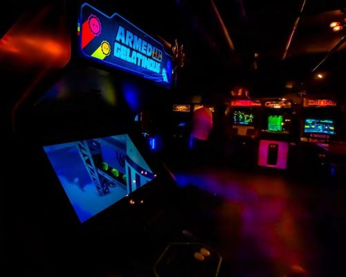 A dimly lit arcade featuring a colorful "Armed and Gelatinous" game cabinet with glowing screens and retro decor.