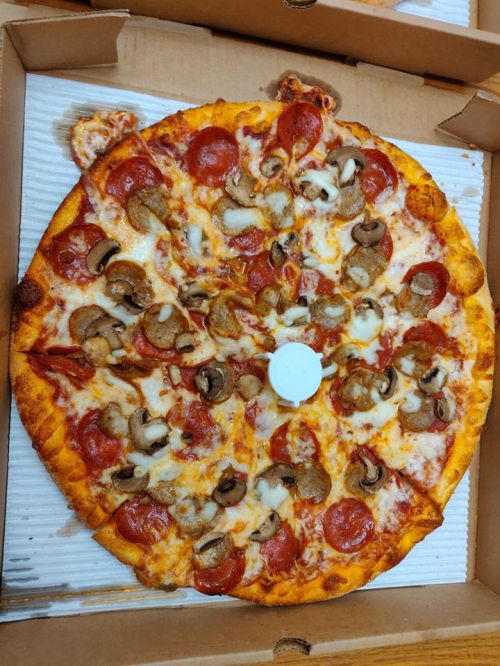 A large pepperoni and mushroom pizza in a pizza box, with a white pizza saver in the center.