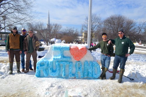 Group of five people standing by a large snow sculpture that says "I ❤️ RUTLAND" on a sunny winter day.