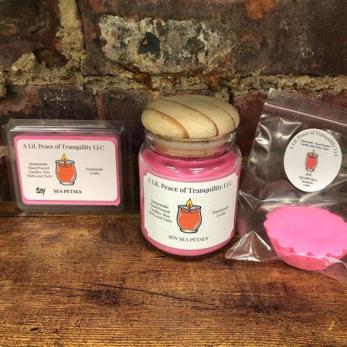 A pink candle in a jar with a wooden lid, alongside wax melts and a label for A Lil' Peace of Tranquility LLC.