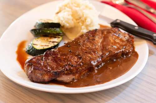 A plate featuring a juicy steak with gravy, grilled zucchini, and creamy mashed potatoes.
