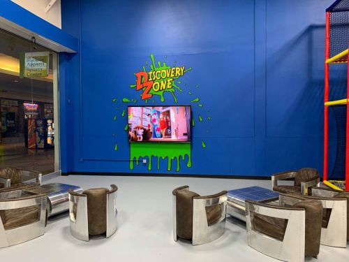 Colorful "Discovery Zone" wall with a TV and modern seating area in a playful indoor space.