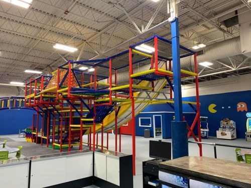 Colorful indoor play structure with slides and climbing areas, set in a spacious, brightly lit play area.
