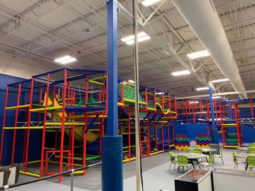 A colorful indoor playground with climbing structures, slides, and play areas, surrounded by tables and chairs.