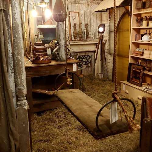A rustic interior featuring a swing, vintage decor, and warm lighting, set in a cozy, straw-filled space.