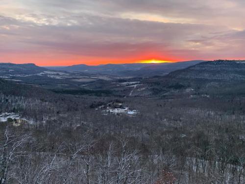 A winter sunset over a valley, with snow-covered trees and distant mountains under a colorful sky.