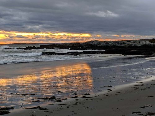 A serene beach scene at sunset, with waves lapping at the shore and colorful reflections on the wet sand.