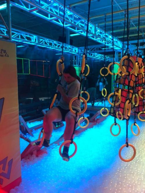A person swings on rings above a colorful ball pit in a vibrant indoor play area.