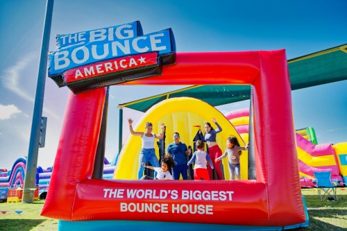 A colorful inflatable bounce house with people joyfully posing in front of a sign that reads "The Big Bounce America."
