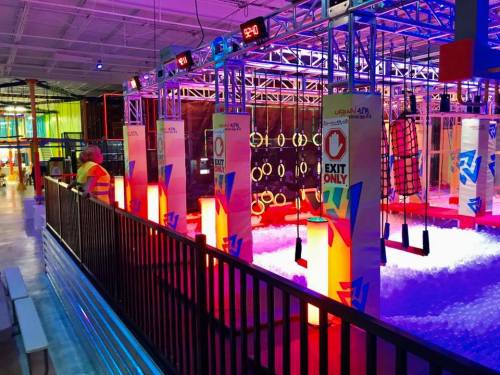 Colorful indoor play area featuring obstacle courses, neon lights, and a ball pit. Safety staff visible in the background.