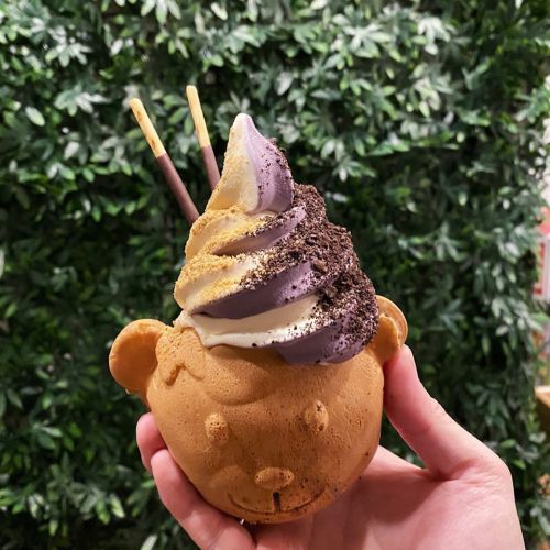 A hand holding a bear-shaped ice cream cup filled with swirled soft serve and topped with crushed cookies.
