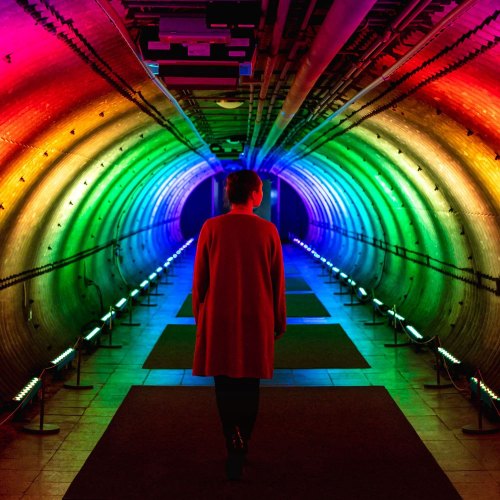 A person walks through a colorful, illuminated tunnel with vibrant rainbow lights along the walls.