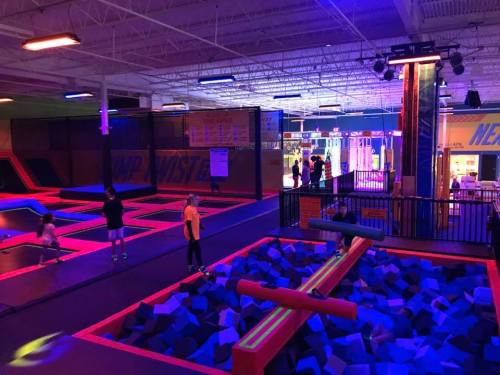 A vibrant indoor trampoline park with colorful lights, featuring trampolines and foam pits, and kids playing.