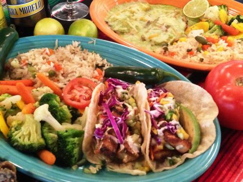 A colorful spread of Mexican food featuring tacos, rice, vegetables, and lime, served on vibrant plates.