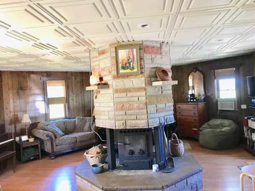 Cozy living room featuring a stone fireplace, patterned ceiling, and comfortable seating with wooden accents.
