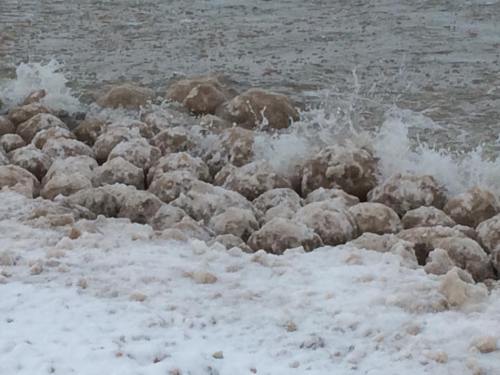Waves crashing against a rocky shoreline covered in white foam and snow-like residue.