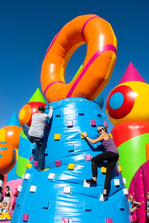 Two people climbing an inflatable structure with colorful designs against a clear blue sky.