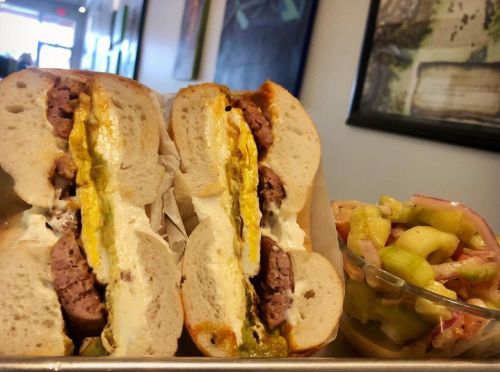 A close-up of a sandwich filled with sausage and mustard, served with a side of colorful pickled vegetables.