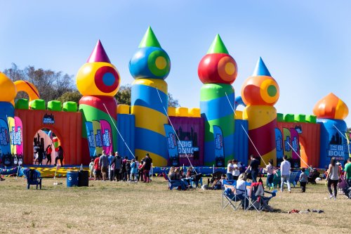 Colorful inflatable bounce house with large towers, surrounded by people and chairs on a grassy field.