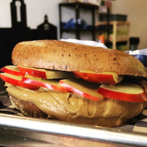 A whole grain bagel filled with peanut butter and topped with apple slices.