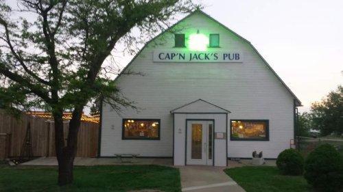 A white barn-style building with a sign reading "Cap'n Jack's Pub" and a green light on the roof, surrounded by trees.