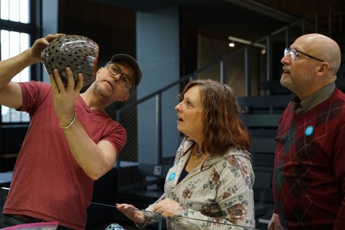A group of three people examines a decorative object in a modern gallery setting, showing curiosity and interest.