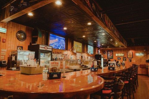 A cozy bar interior with a wooden counter, beer taps, and TVs displaying sports, creating a welcoming atmosphere.