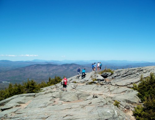 Hikers on a rocky mountain summit with a clear blue sky and distant mountains in the background.