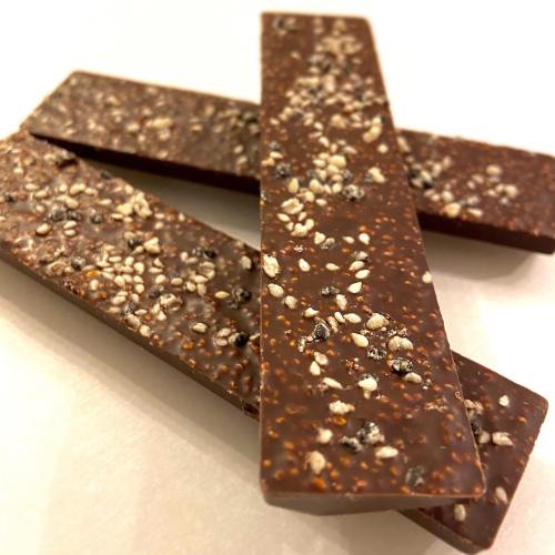 Three chocolate bars with a textured surface, sprinkled with seeds, arranged on a light background.