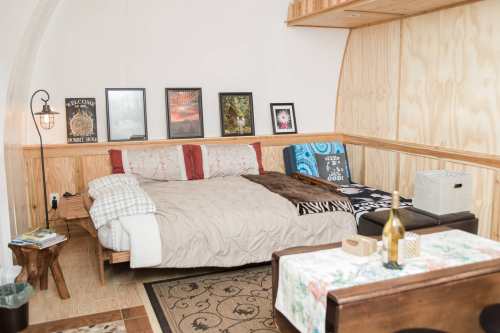 Cozy bedroom with a wooden accent wall, a large bed, framed art, and a small dining table with a wine bottle.