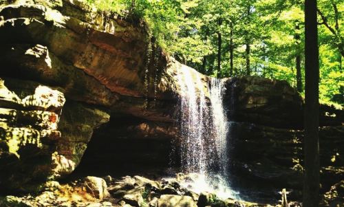 A serene waterfall cascading over rocky cliffs, surrounded by lush green trees in a tranquil forest setting.