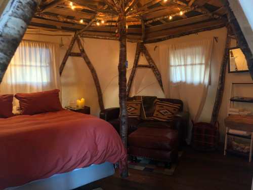 Cozy interior of a rustic cabin with a bed, armchair, and warm lighting from string lights.