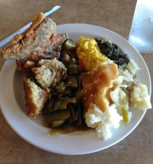 A plate of Southern comfort food featuring fried chicken, cornbread, greens, mashed potatoes, and mixed vegetables.