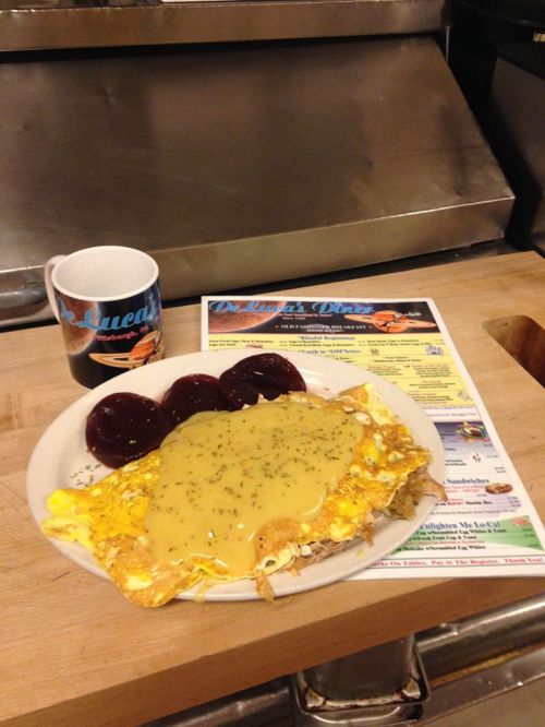 A plate of eggs topped with gravy, served with three jelly-filled pastries and a coffee mug, on a wooden table.