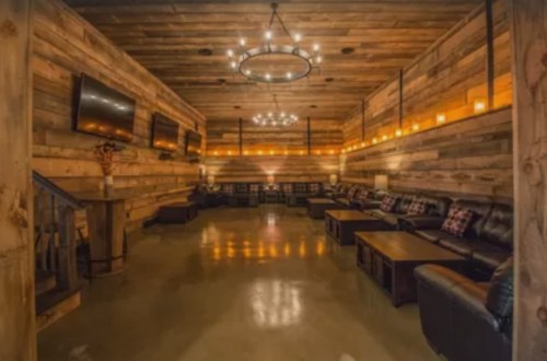 Cozy lounge with wooden walls, leather seating, and warm lighting from chandeliers and candles.