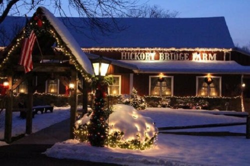 A cozy farm building adorned with holiday lights, surrounded by snow and festive decorations at dusk.