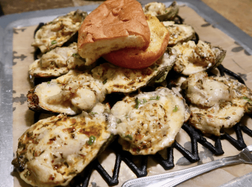 Grilled oysters topped with herbs and cheese, served on a platter with a bun on top.