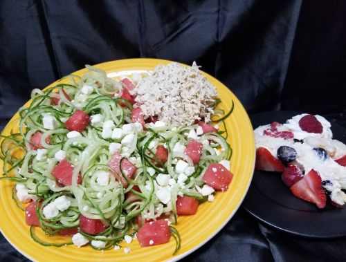 A vibrant plate of spiralized zucchini salad with watermelon, feta, and a side of shredded chicken and mixed berry dessert.
