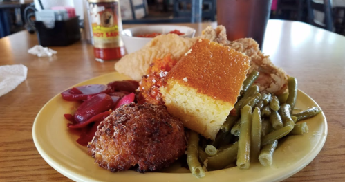 A plate of Southern comfort food featuring fried chicken, cornbread, green beans, pickled beets, and a side of hot sauce.