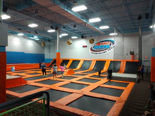 A vibrant trampoline park with orange trampolines and people jumping and playing in a spacious indoor area.